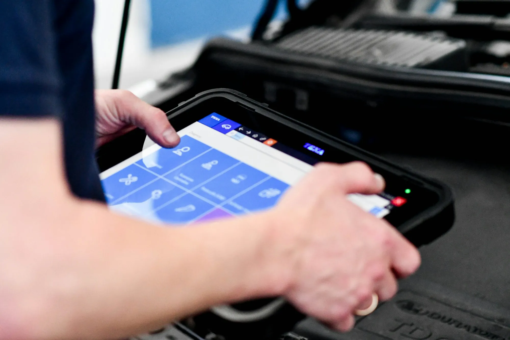 Technician holding a diagnostic tablet near an open engine